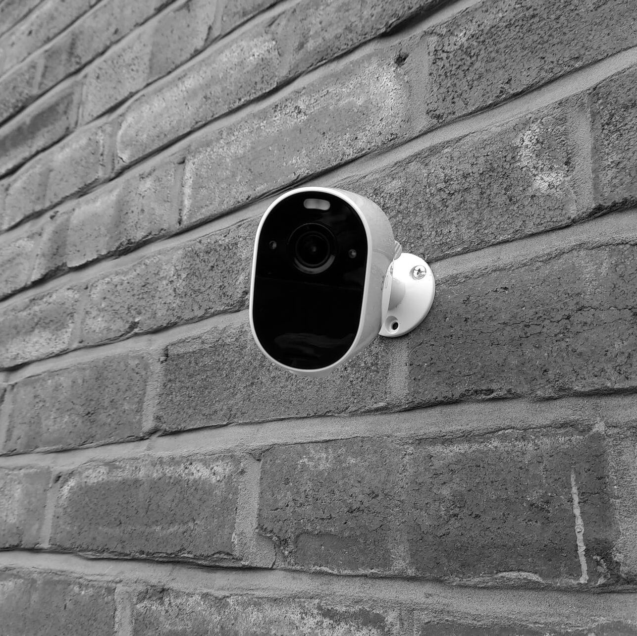monochrome photo of a surveillance camera on a brick wall